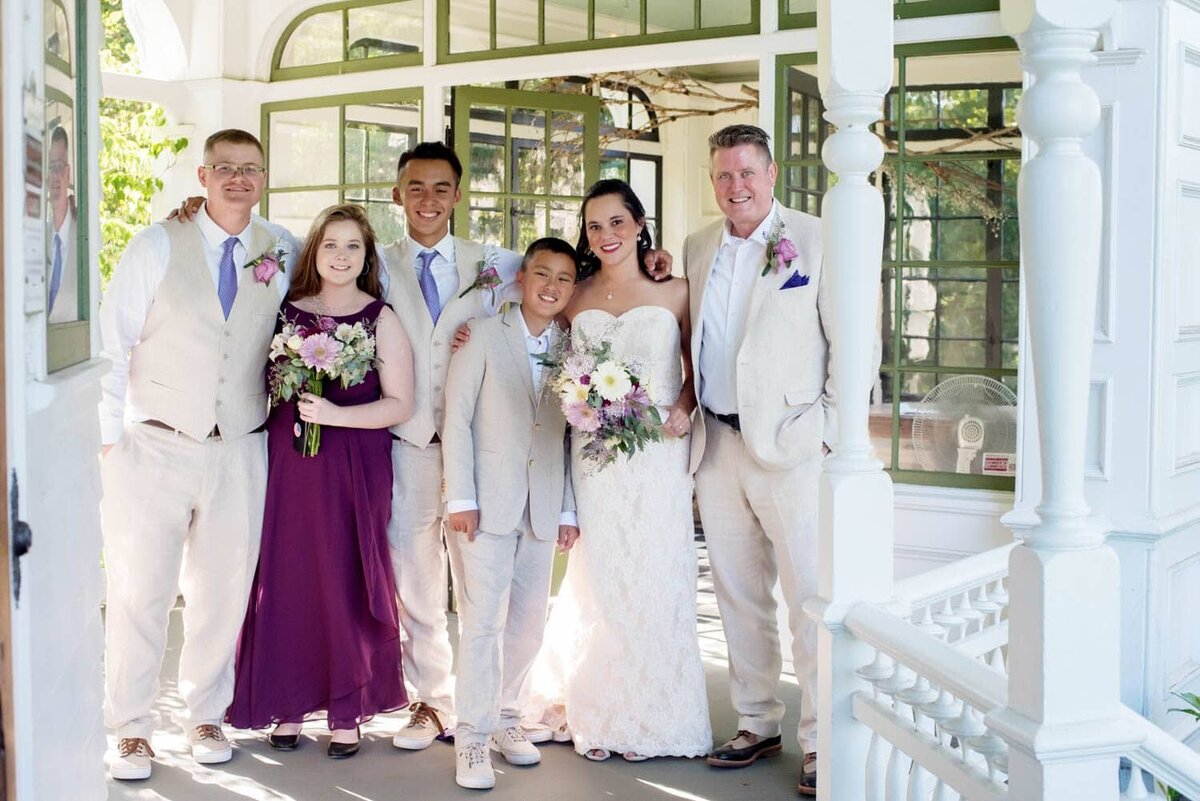 a wedding party hugs around each other in front of the sun room on the porch of deepwood