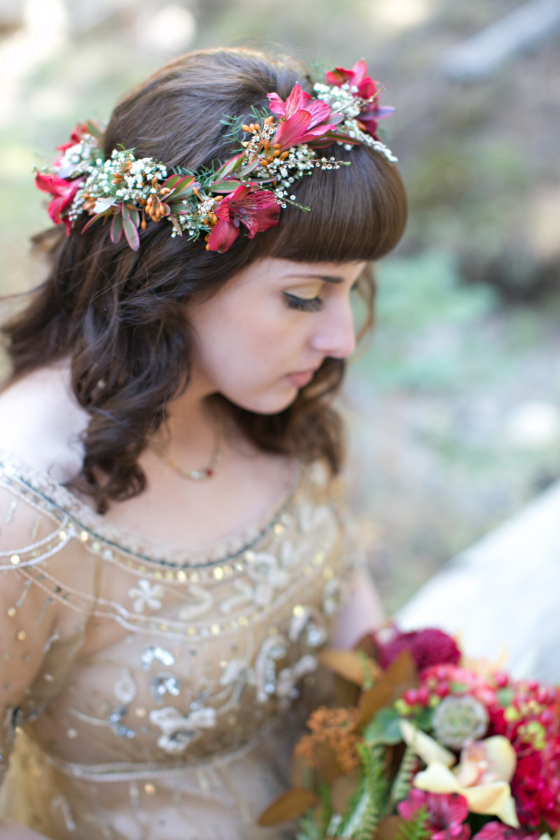 Bride wearing floral crown and wearing gold wedding dress looking down at bouquet