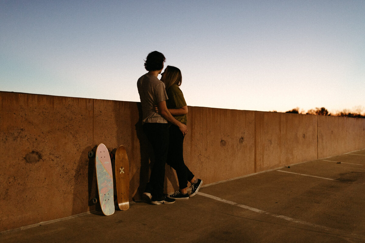 Couple standing next to their skateboards on top of a parking garage at dusk