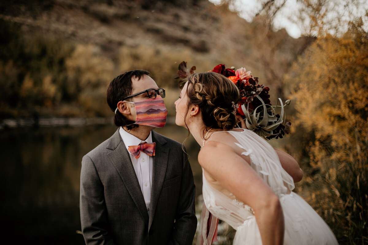 bride leaning in to kiss groom with a mask on