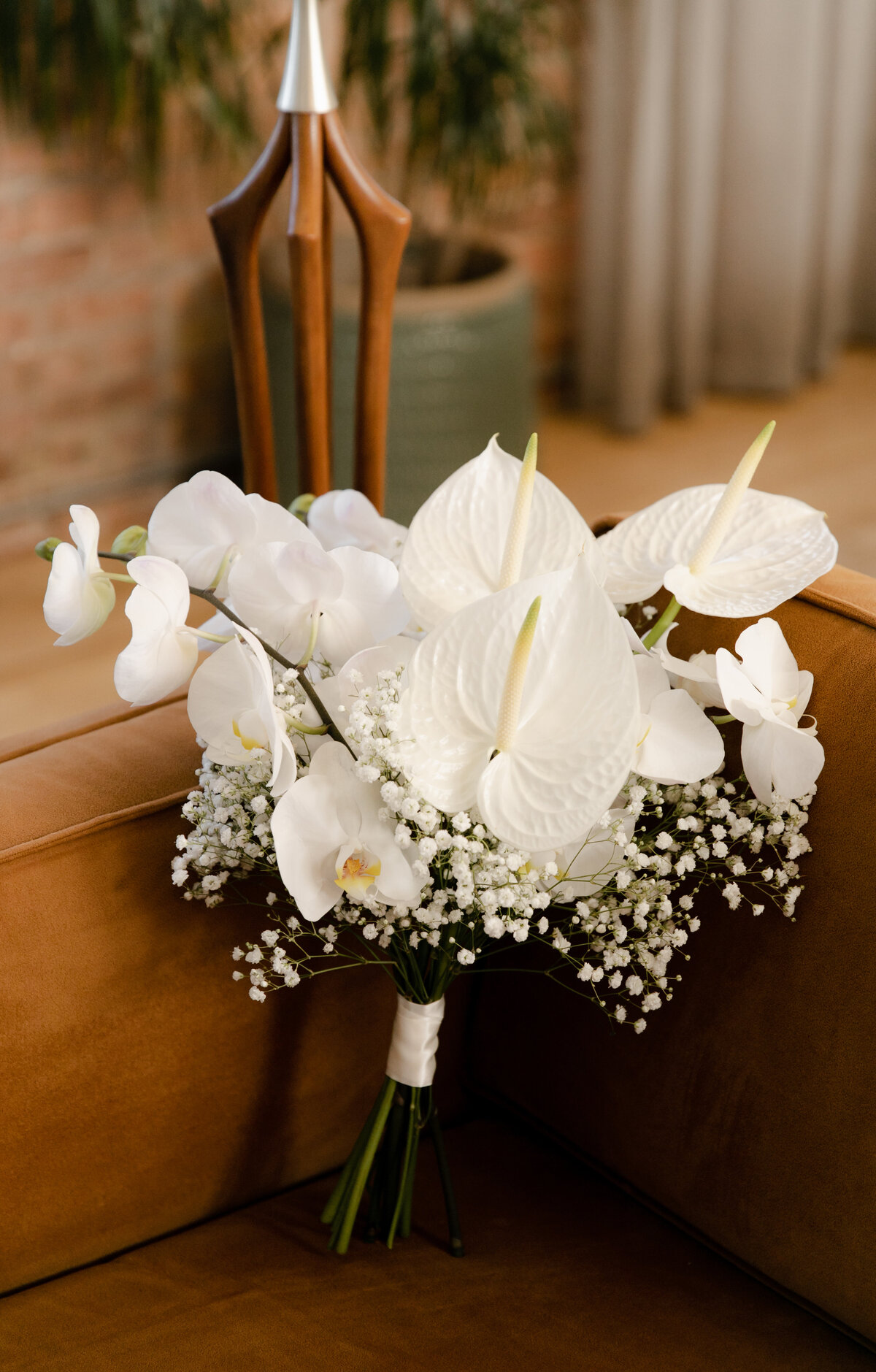 White lilies and baby's breath wedding  bouquet pictured atop brown leather couch at Moody Tongue Brewery in Chicago.