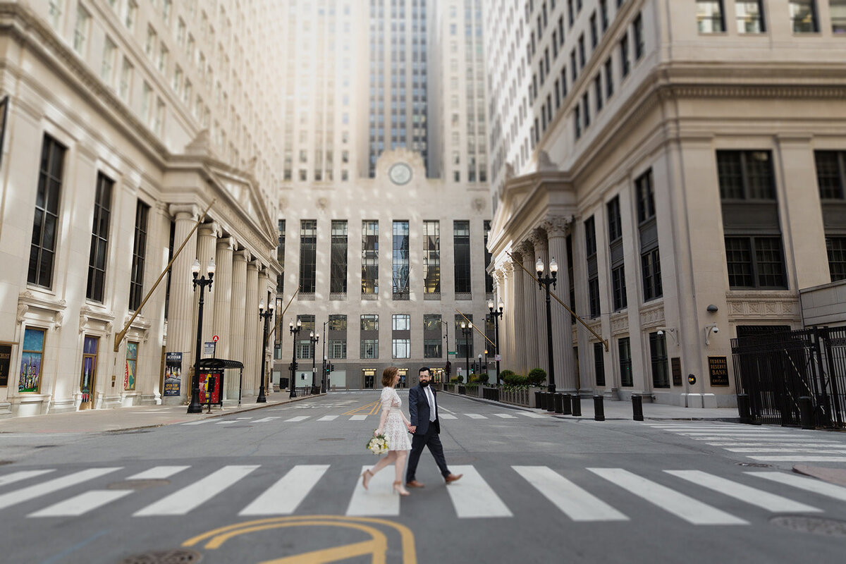 Elopement couple crosses LaSalle Street in Chicago with the Chicago Board of Trade in the background