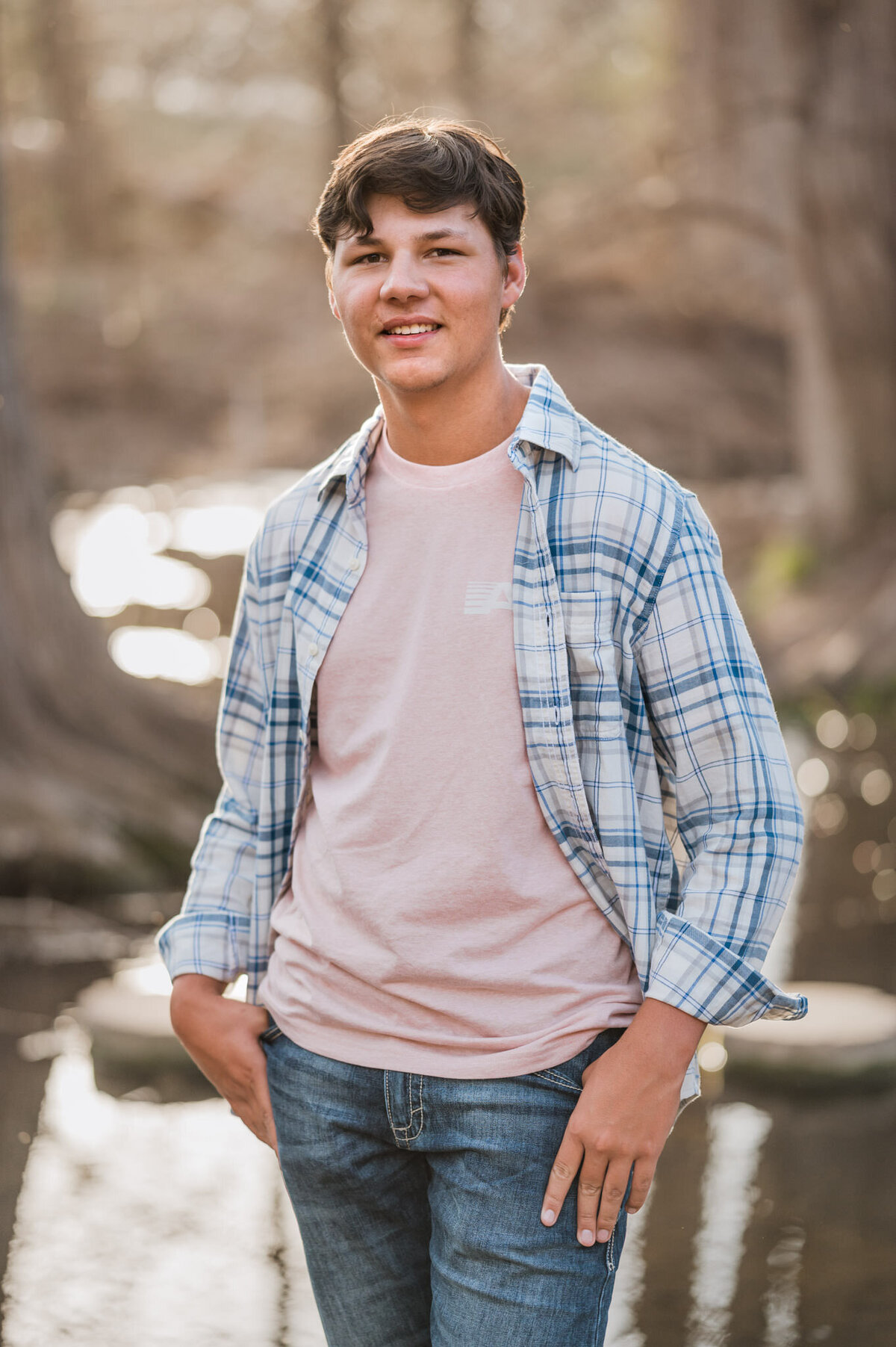 Senior guy stands in front of a creek during golden hour senior pictures.