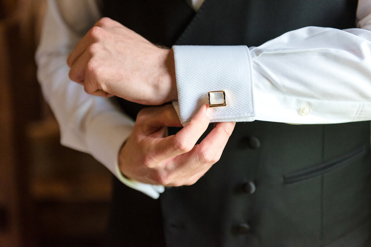 A close-up of a man's hands fastening a cufflink on a dress shirt sleeve.