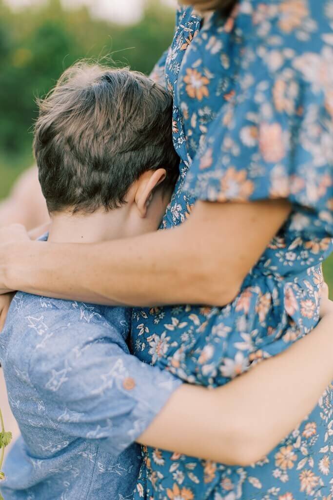 Close up photo of a mother in a teal flower gown and son share a sweet moment hugging each other.