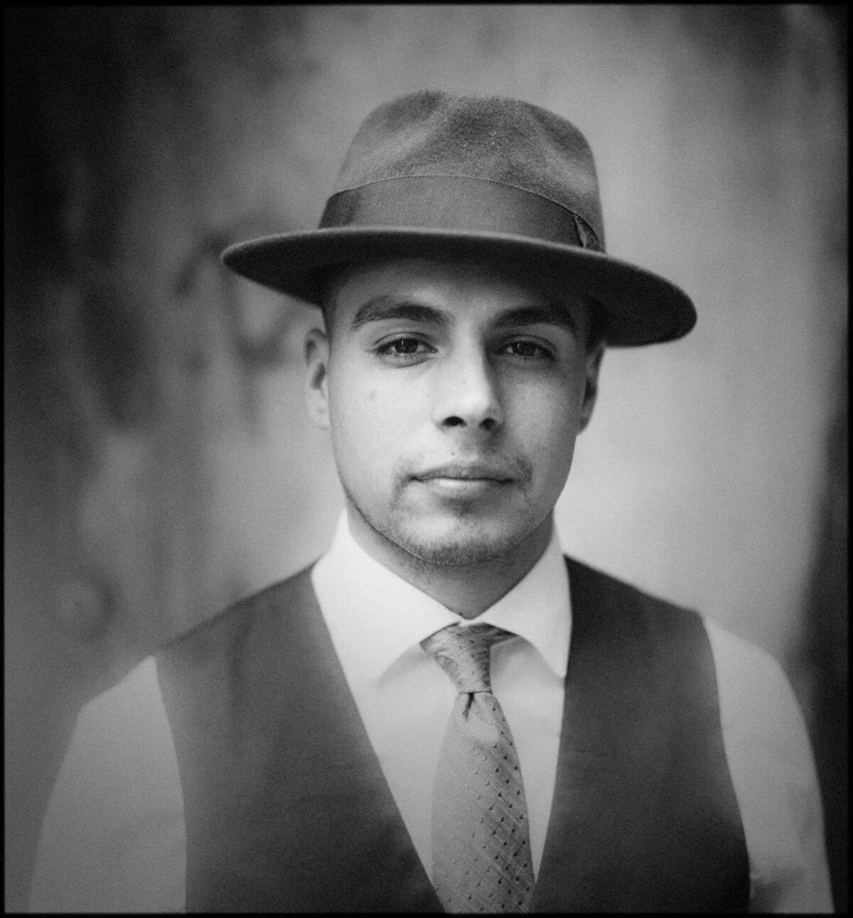 A man in a hat and suit with a small smile
