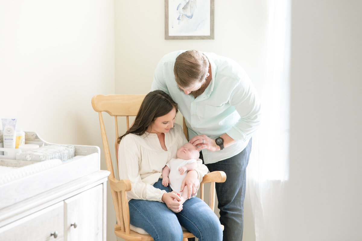 new mom and dad in rocking chair with their new baby in nursery