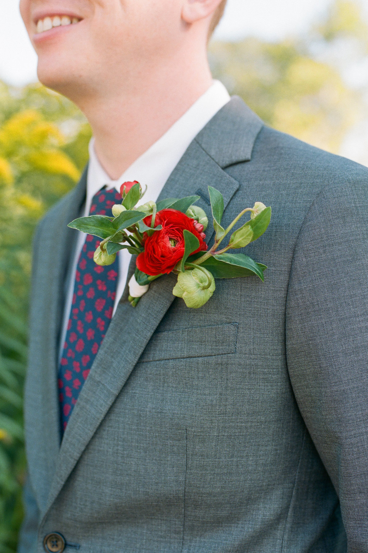 groom in grey suit with red and green boutonniere