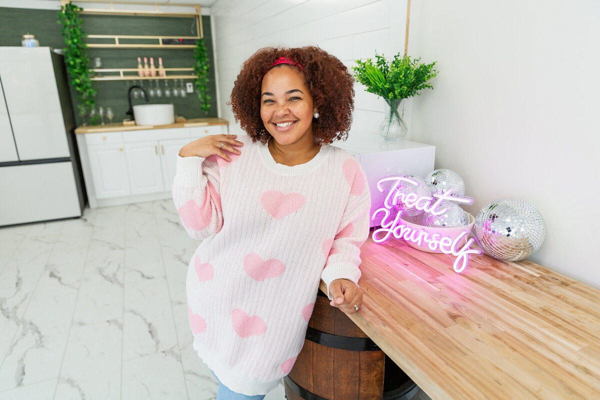 A-venue-owner-smiles-next-to-a-treat-yourself-sign-during-her-baltimore-branding-session