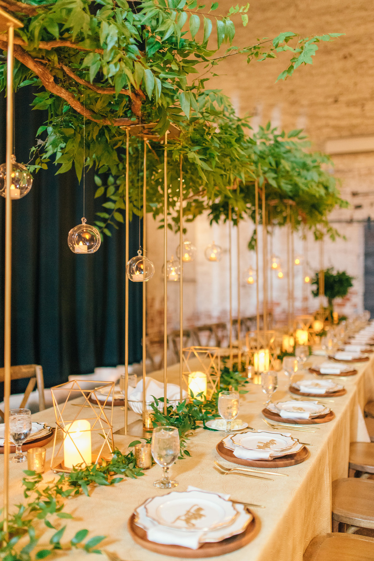 long headtable with tall greenery centerpieces on gold stands with hanging orbs for lighting