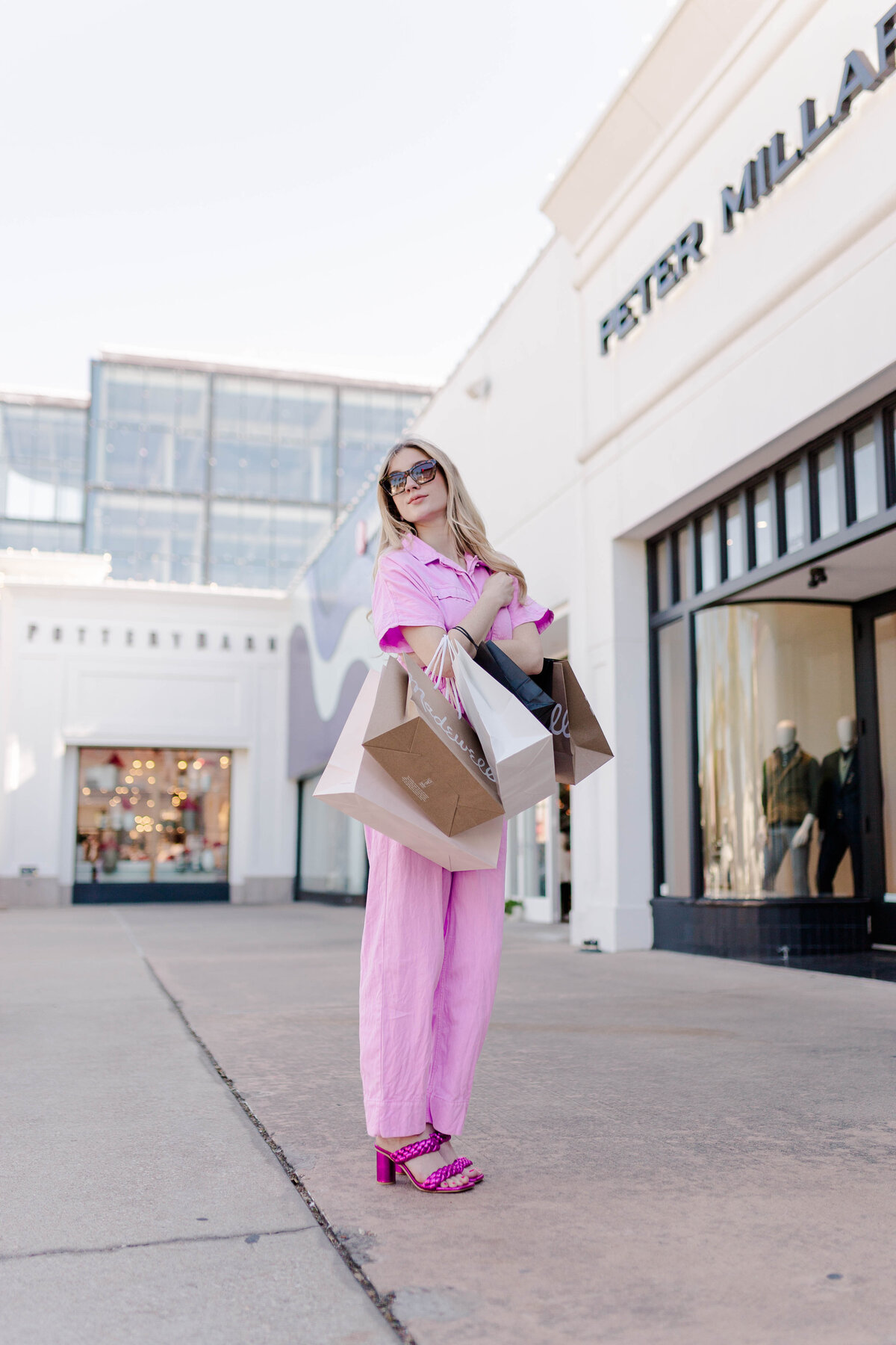 Fashion barbie poses with shopping bags in a pink jumpsuit in front of pottery barn in houston