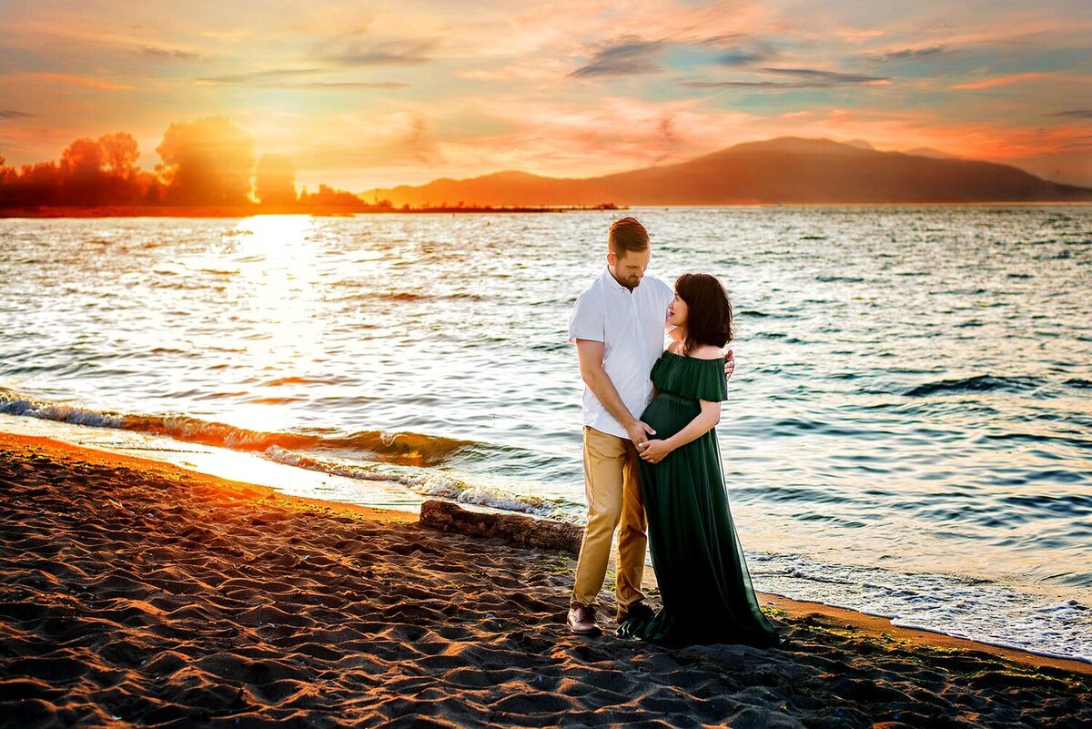 Pregnant woman in emerald green maternity dress with husband at Jericho Beach in Vancouver at sunset