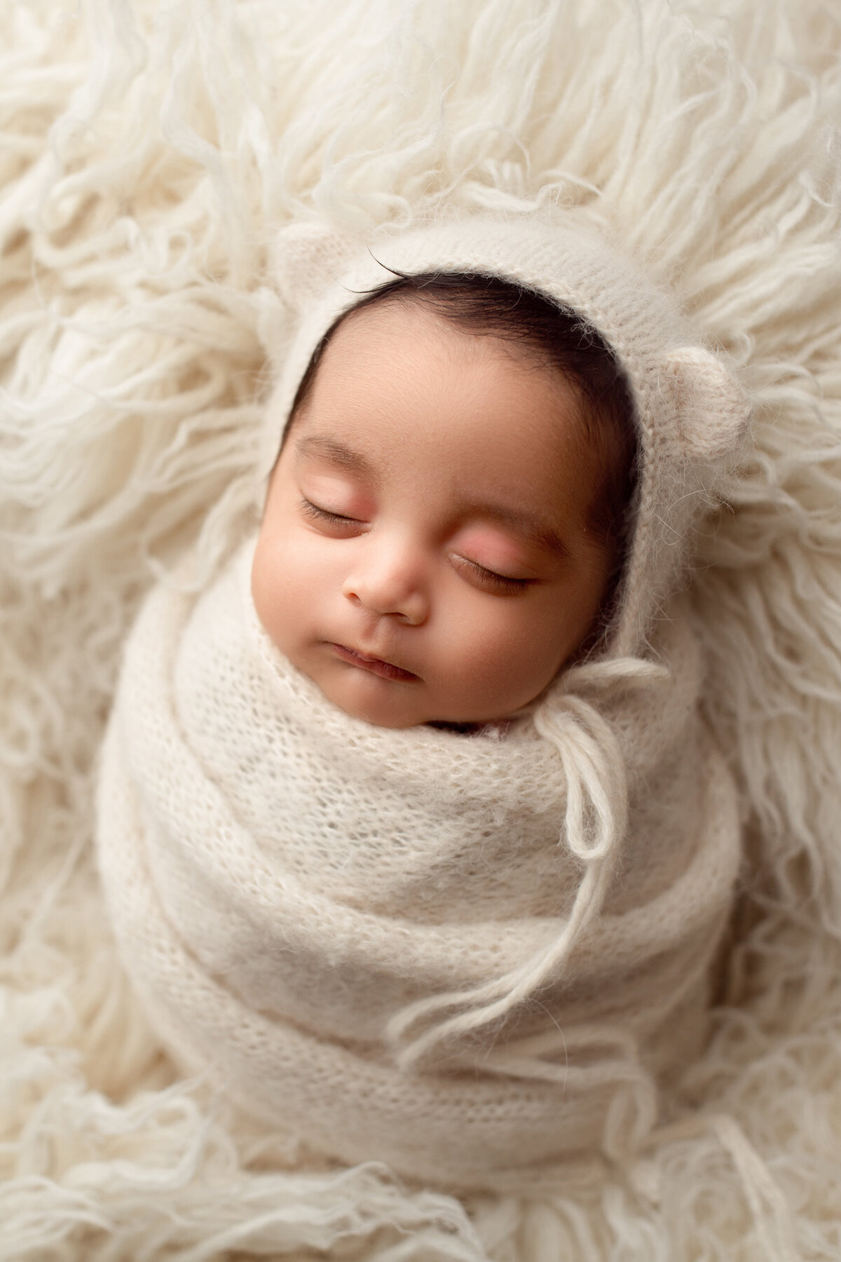 baby boy wrapped in a cream swaddle and wearing a cream bonnet