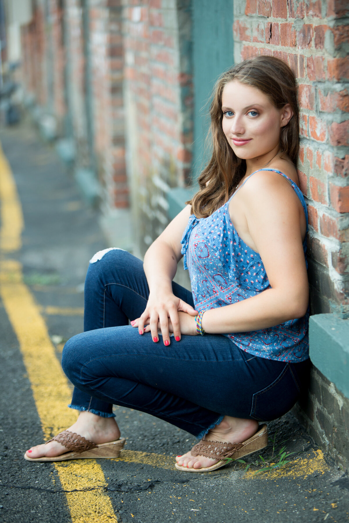 A white teenage girl with dark blonde hair and blue eyes wearing a blue tank top and jeans poses at the Garner Arts Center Suffern senior portrait photographer Milestone Images
