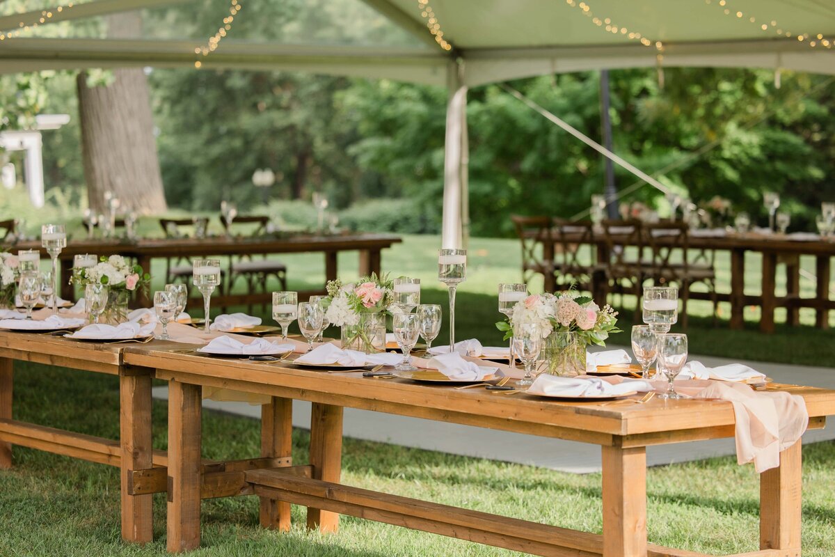 Outdoor wedding reception area under a tent at Park Farm Winery with elegantly set wooden tables, floral centerpieces, and string lights.