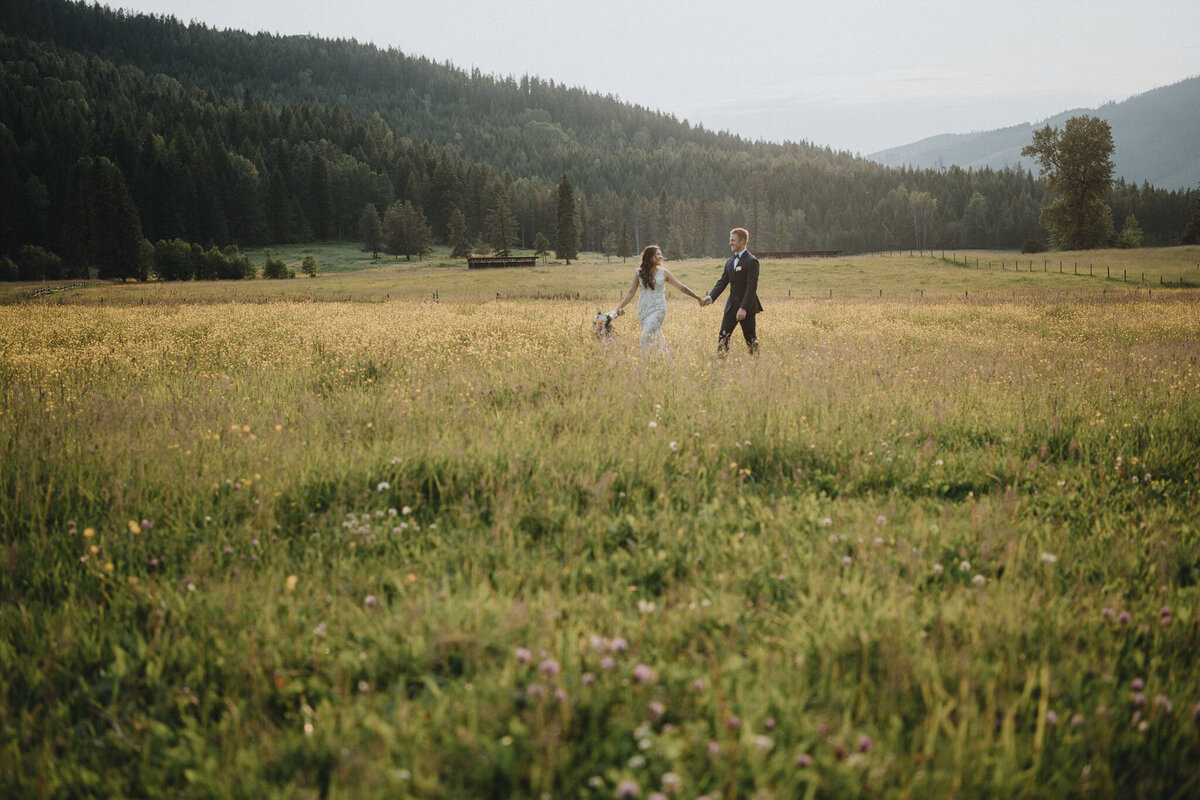 Bride and groom walking holding hands in a field, captured by Photos by Marissa, nostalgic and romantic wedding photographer in Kelowna, BC. Featured on the Bronte Bride Vendor Guide.