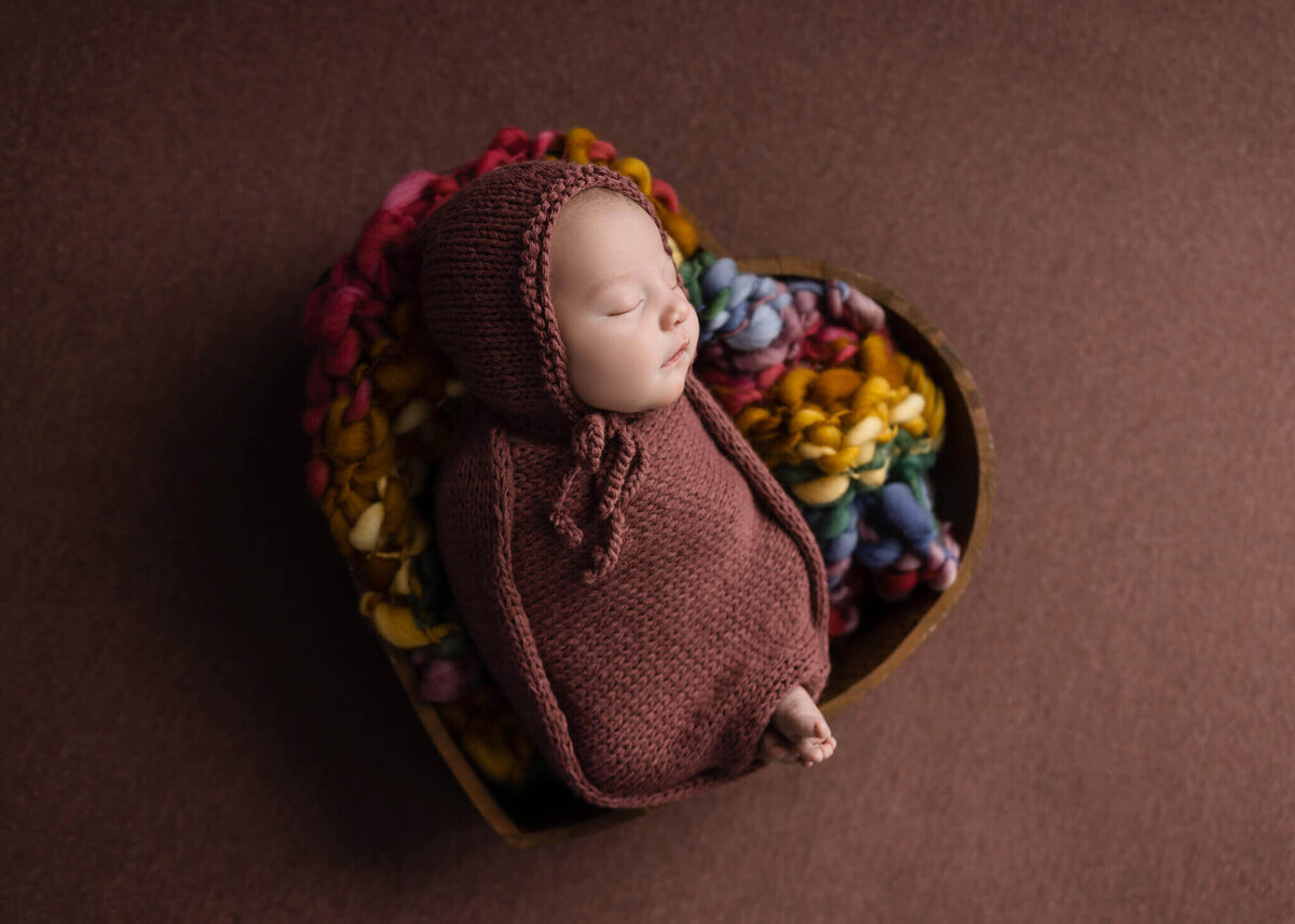 newborn baby in a red knitted wrap asleep in a heart shaped bowl