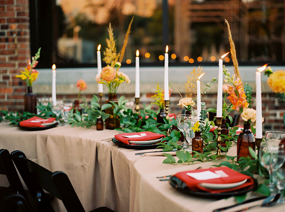 Table set with ivory table cloth, red napkins, candlesticks, and amber glassware with flowers.