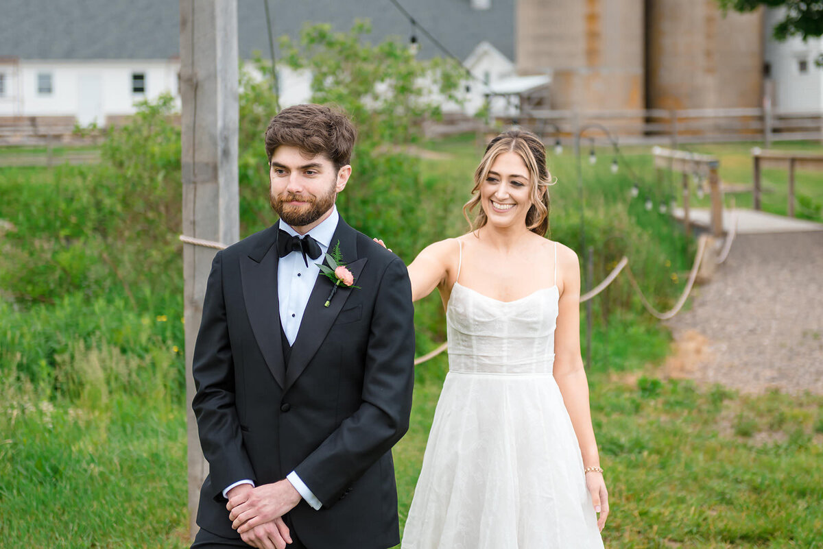 A bride and groom walking side by side on a farm, with the groom looking forward and the bride smiling at the camera.