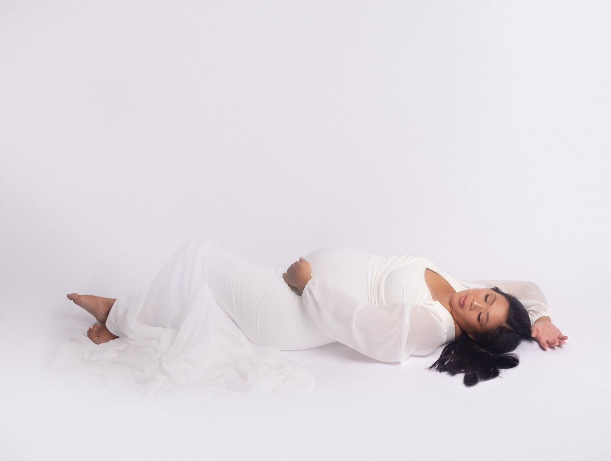 women wearing white gown,  laying on back during maternity photoshoot in Franklin tennessee photography studio