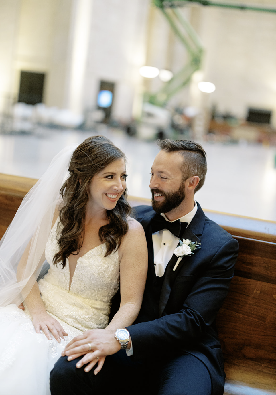 Chicago bride and groom sit on a wooden bench holding hands and smiling at each other.