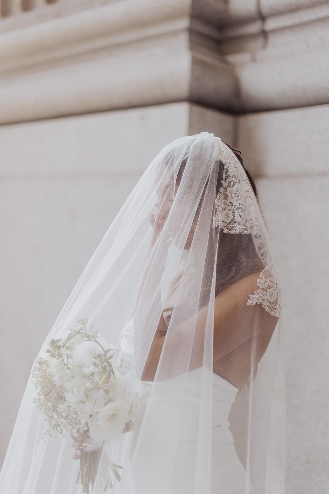 Bride in a white gown with a lace veil holding a bouquet posing for photography