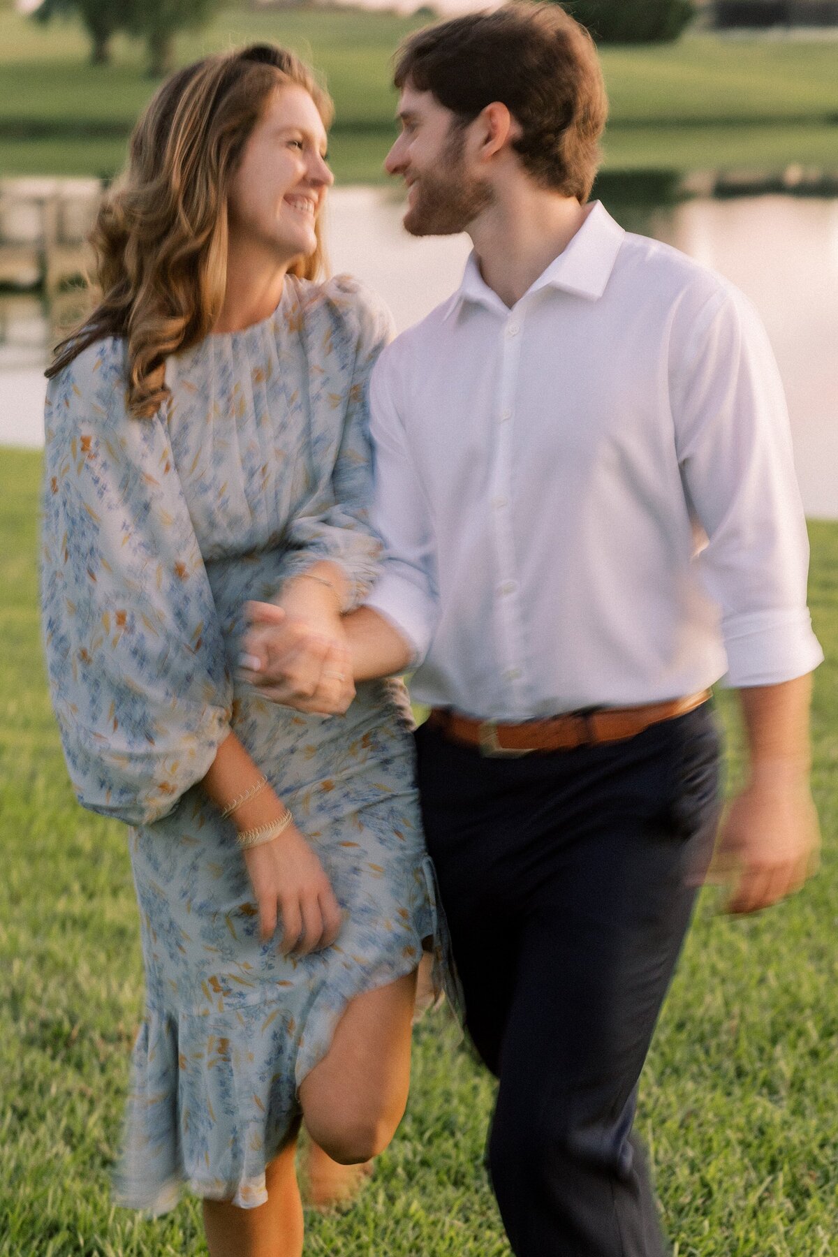 engaged couple smile at each other while walking hand in hand