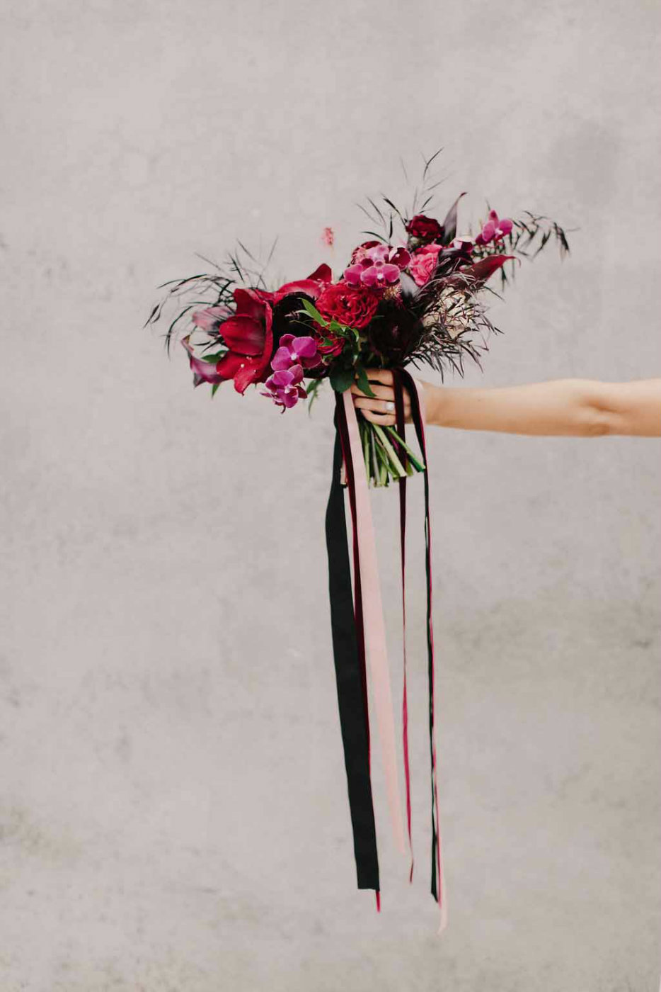 Stunning and unusual bridal bouquet with orchid, red amaryllis, black dahlias, and ranunculus with velvet streamers.