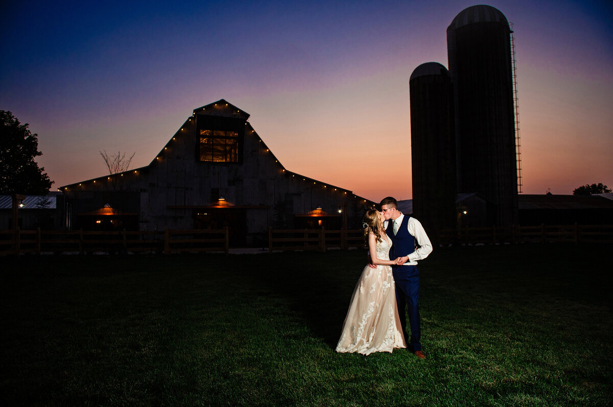 Bride and groom sharing a kiss at sunset with the barn silhouette behind them
