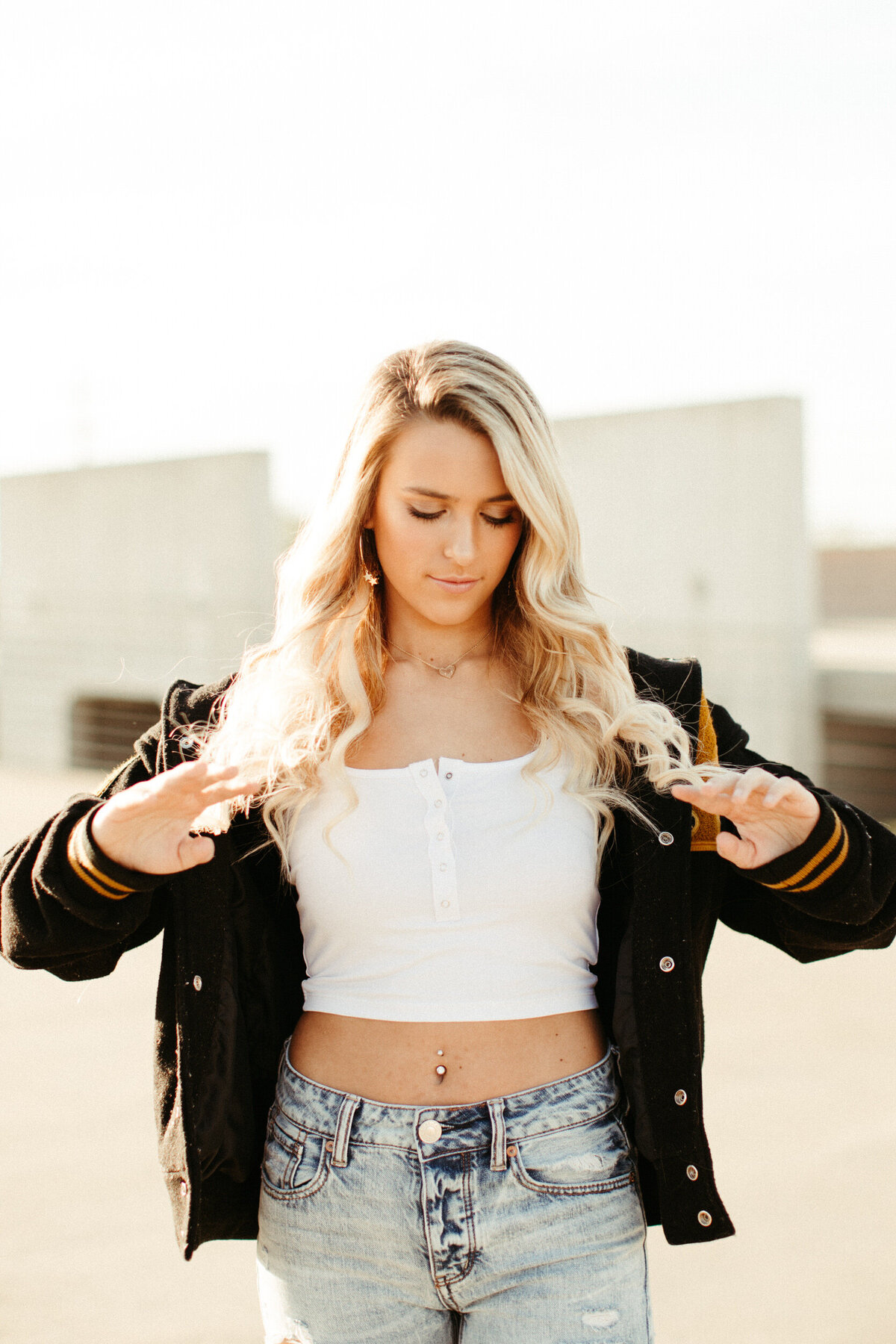 High school senior wearing white crop top and letterman jacket on top of a parking garage