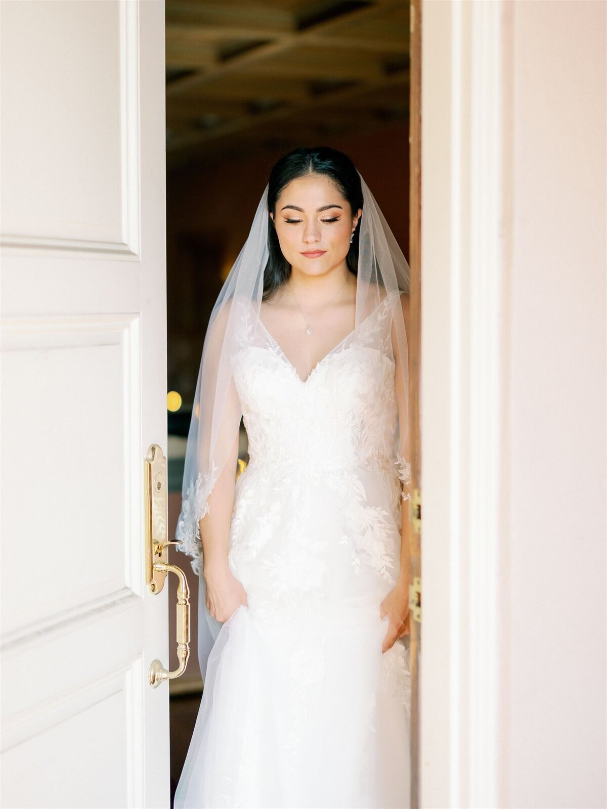 A bride in a white dress stands in the doorway of a room.
