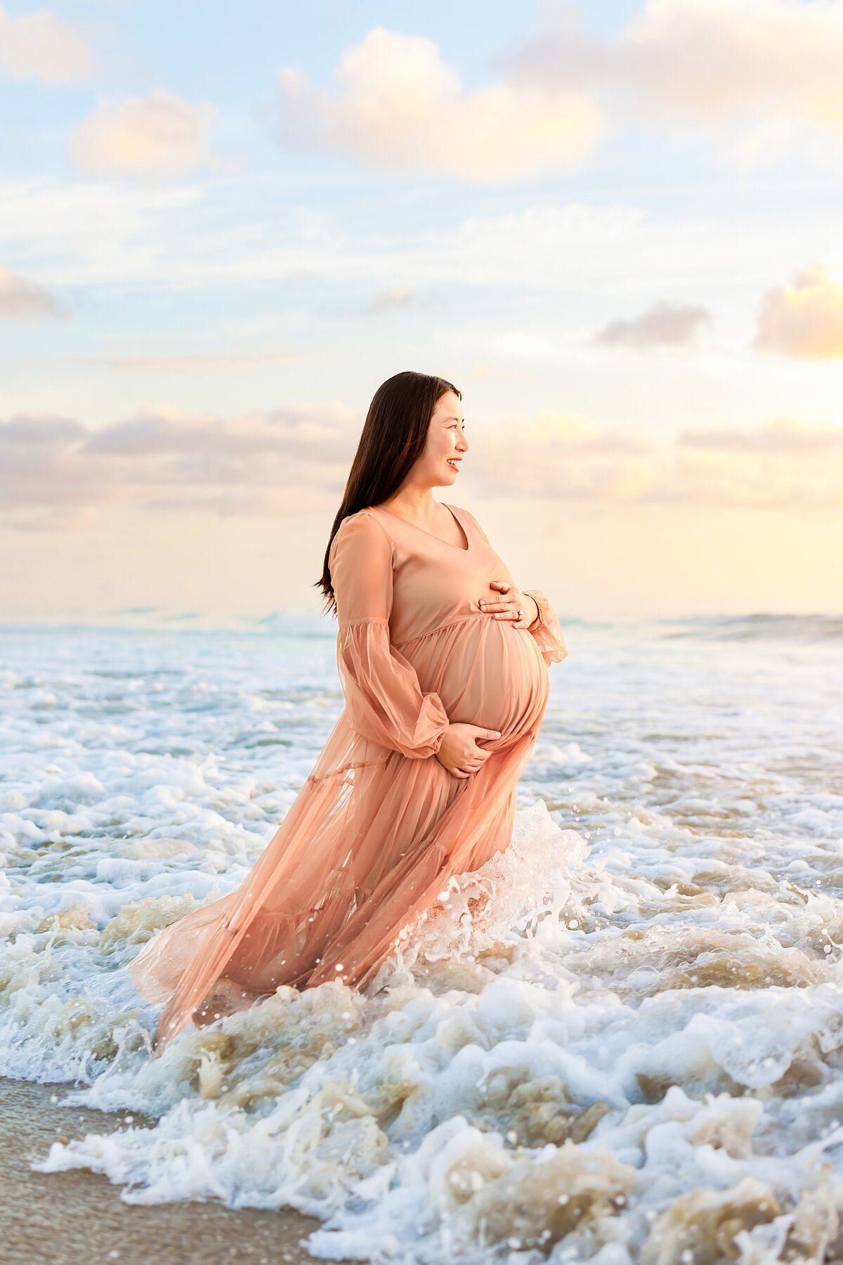 Maternity portrait of woman looking out over the ocean while waves splash around her in San Diego