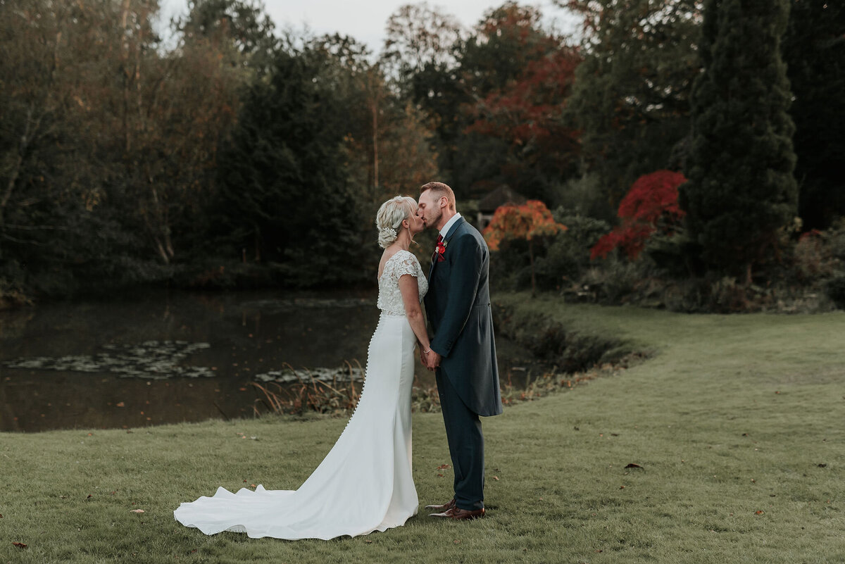 Bride & Groom share a kiss in front of gorgeous Autumn trees at their wedding at The Ravenswood