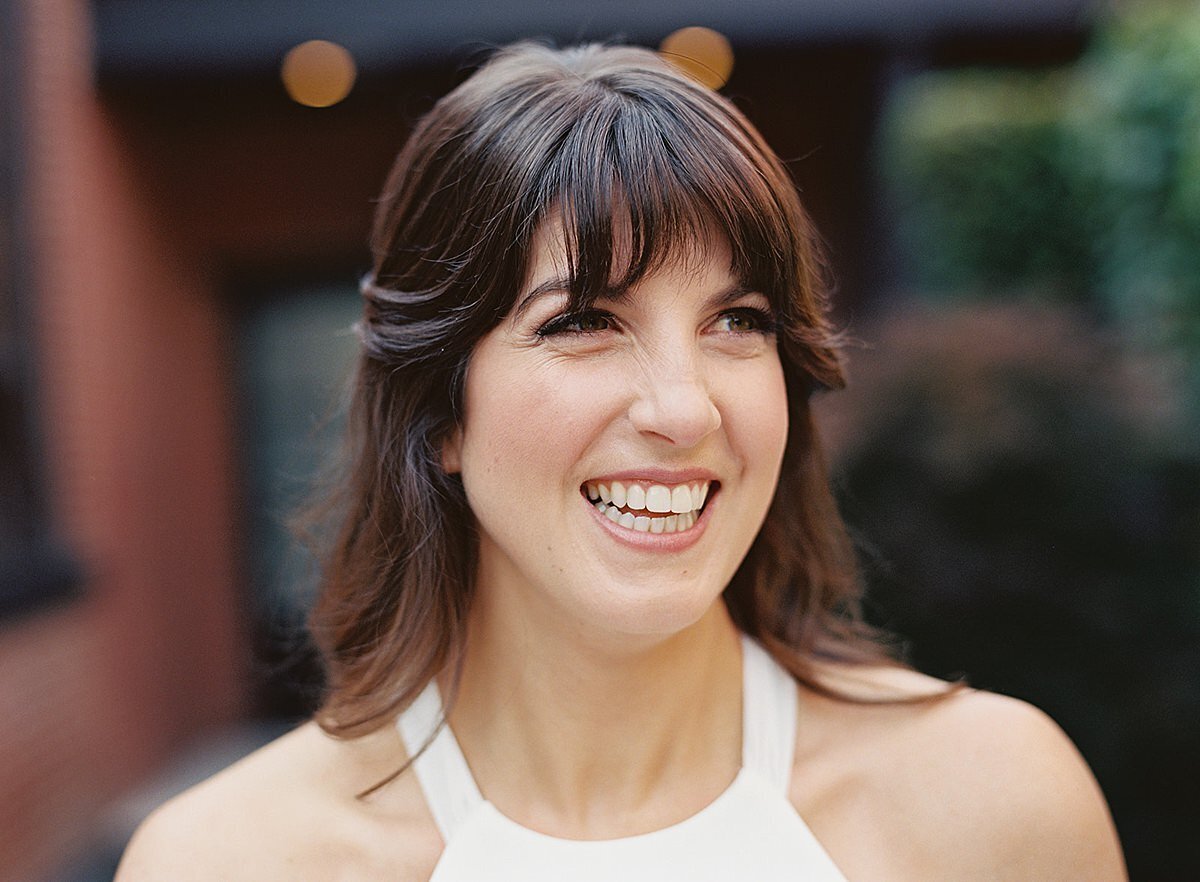 The bride, a brunette in a halter top silk sheath dress smiles at her guests as she walks into the reception at Clementine Hall