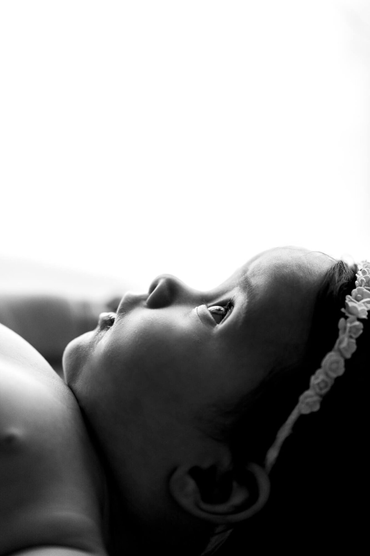 Black and white profile portrait of a baby girl wearing a floral headband laying down and looking up in and OKC studiio.