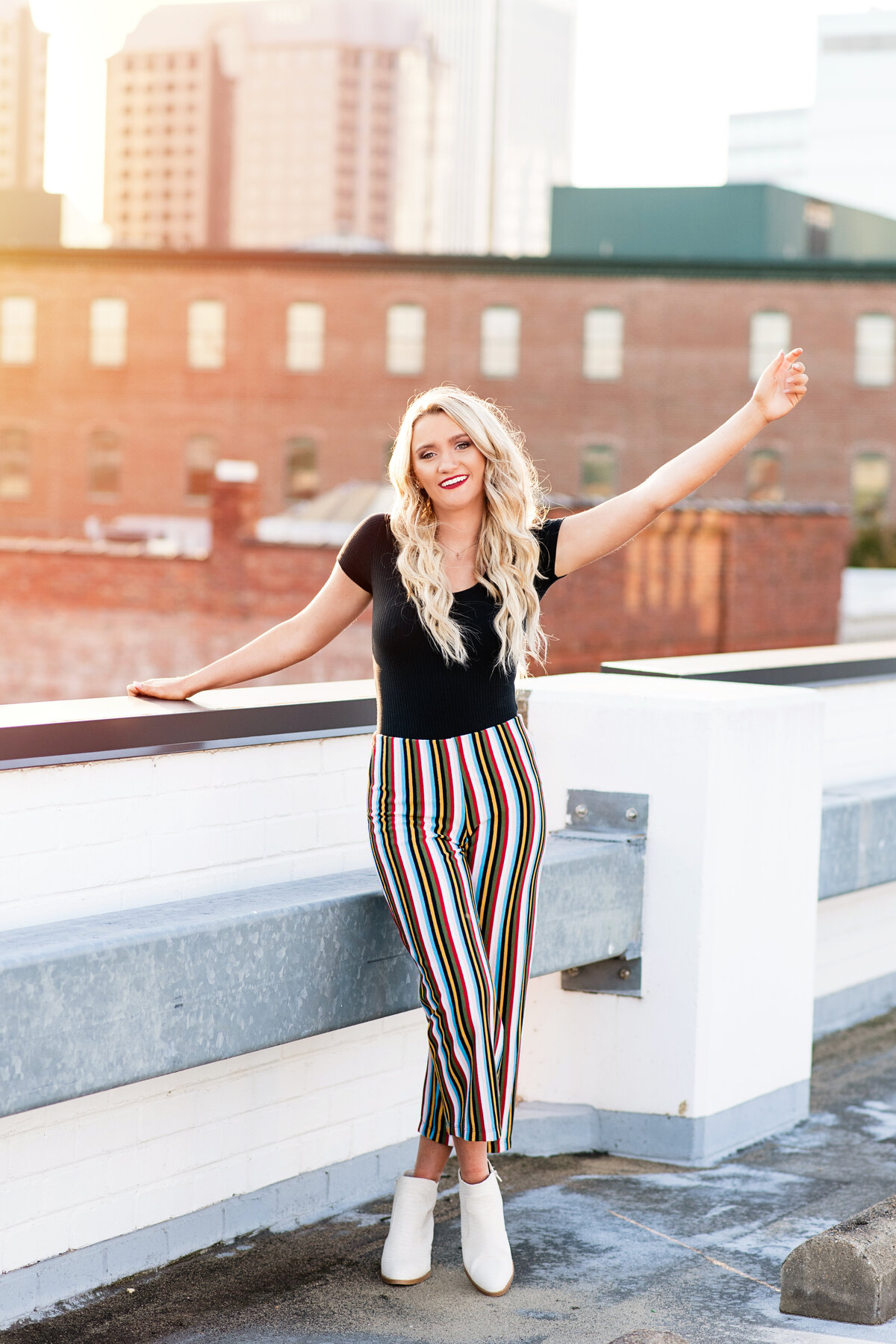 Clover Hill high school girl wearing striped pants waves during her sunset portrait session on a rooftop downtown Richmond, VA.