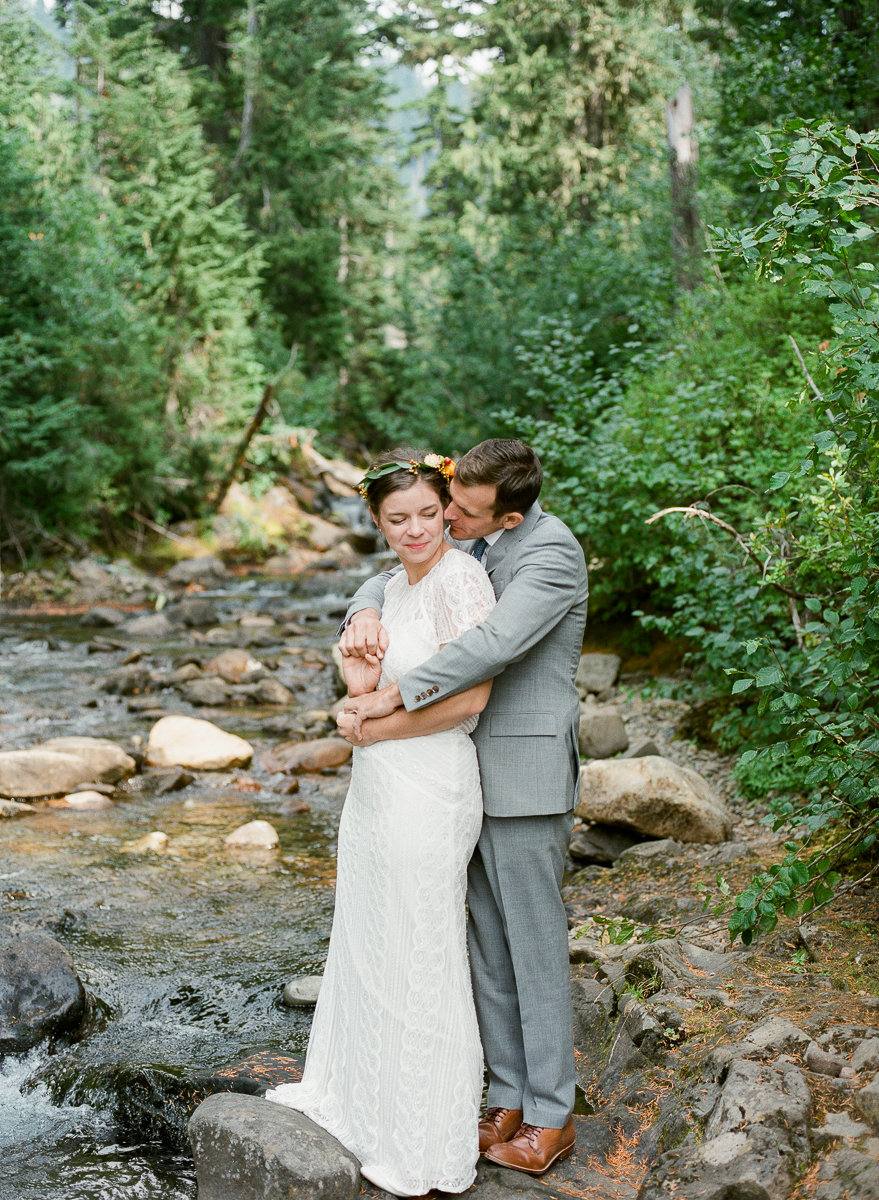 wedding couple stands on rock in the middle of fall mountain stream washington mt rainier