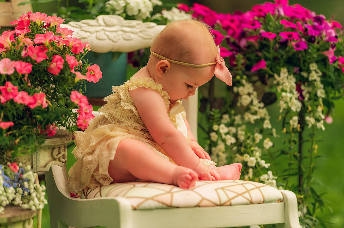 A baby is photographed sitting on a vintage dining chair surrounded by pink flowers in Eagle's Paradise Springs.