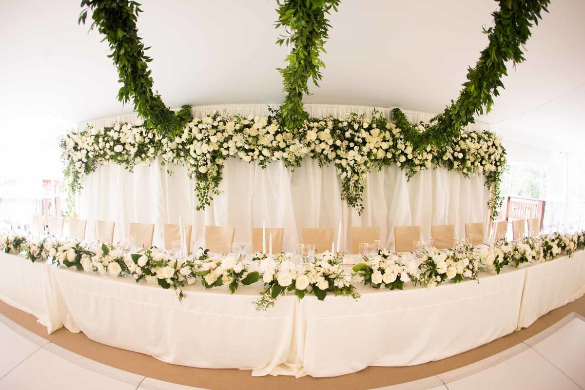 Large white flower wall installation behind head table with green garlands above