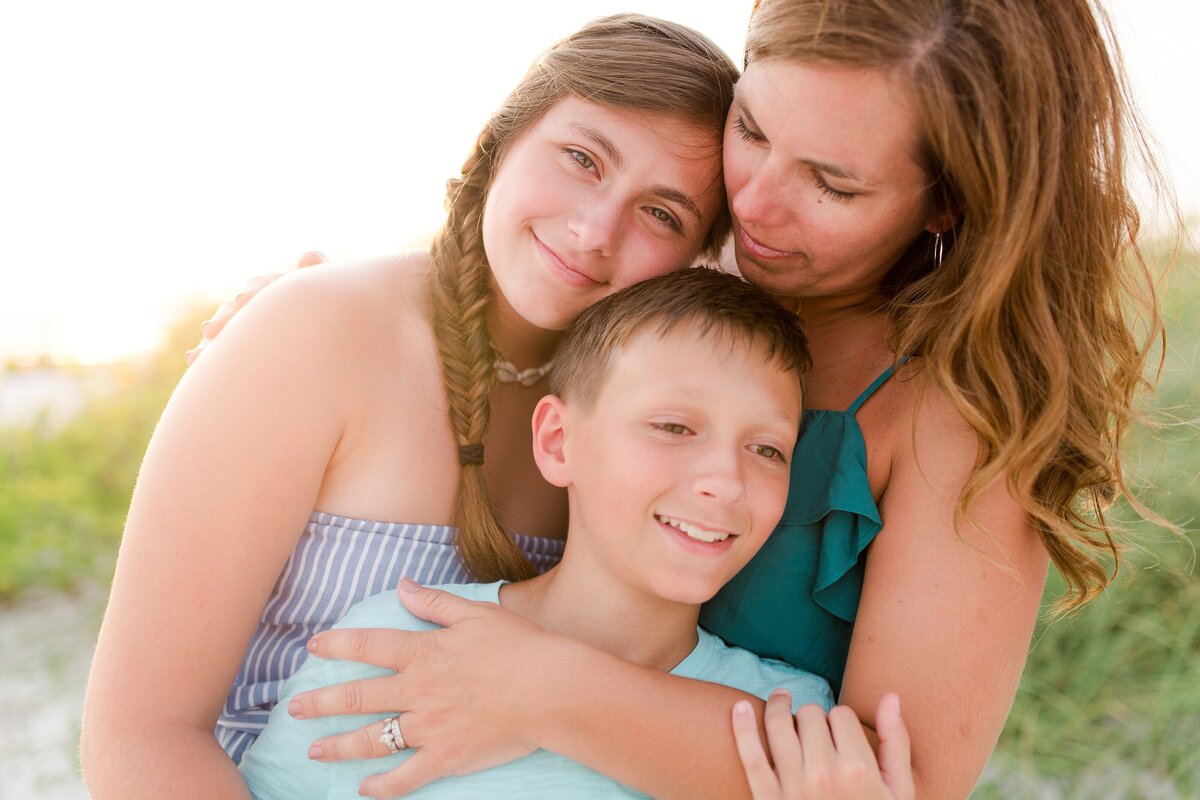 A mom hugging her teenage son and daughter during a family photo session on Honeymood Island FL.