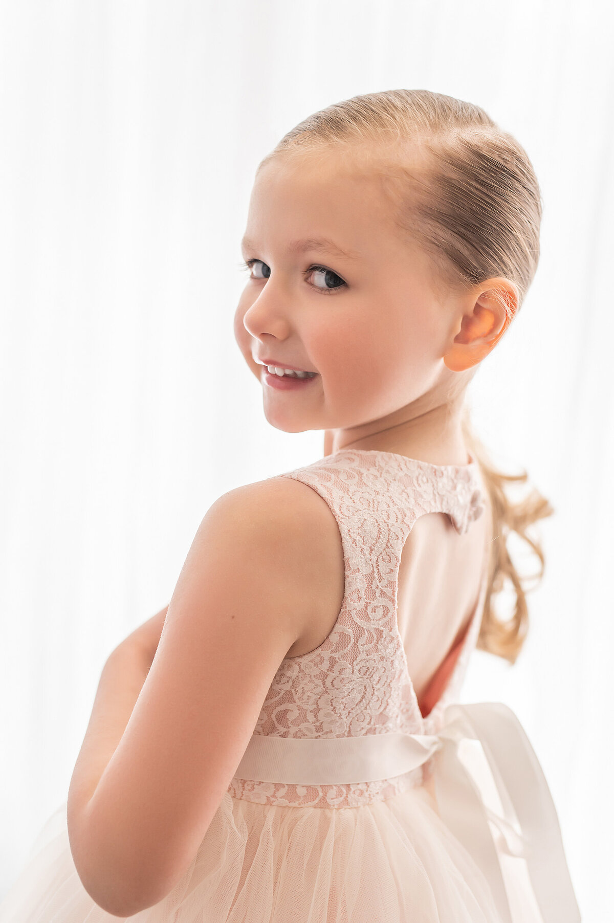 A young girl looks at the camera over her shoulder showing the heart cutout detail in the back of her gown,