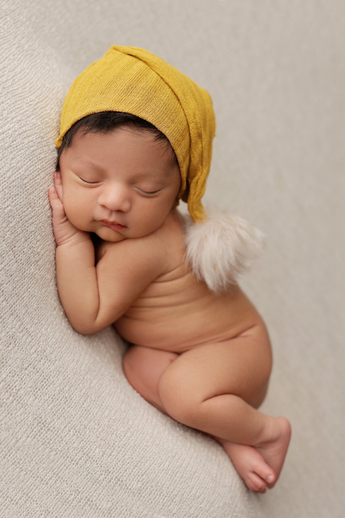 newborn baby boy sleeping on a cream blanket wearing a yellow hat