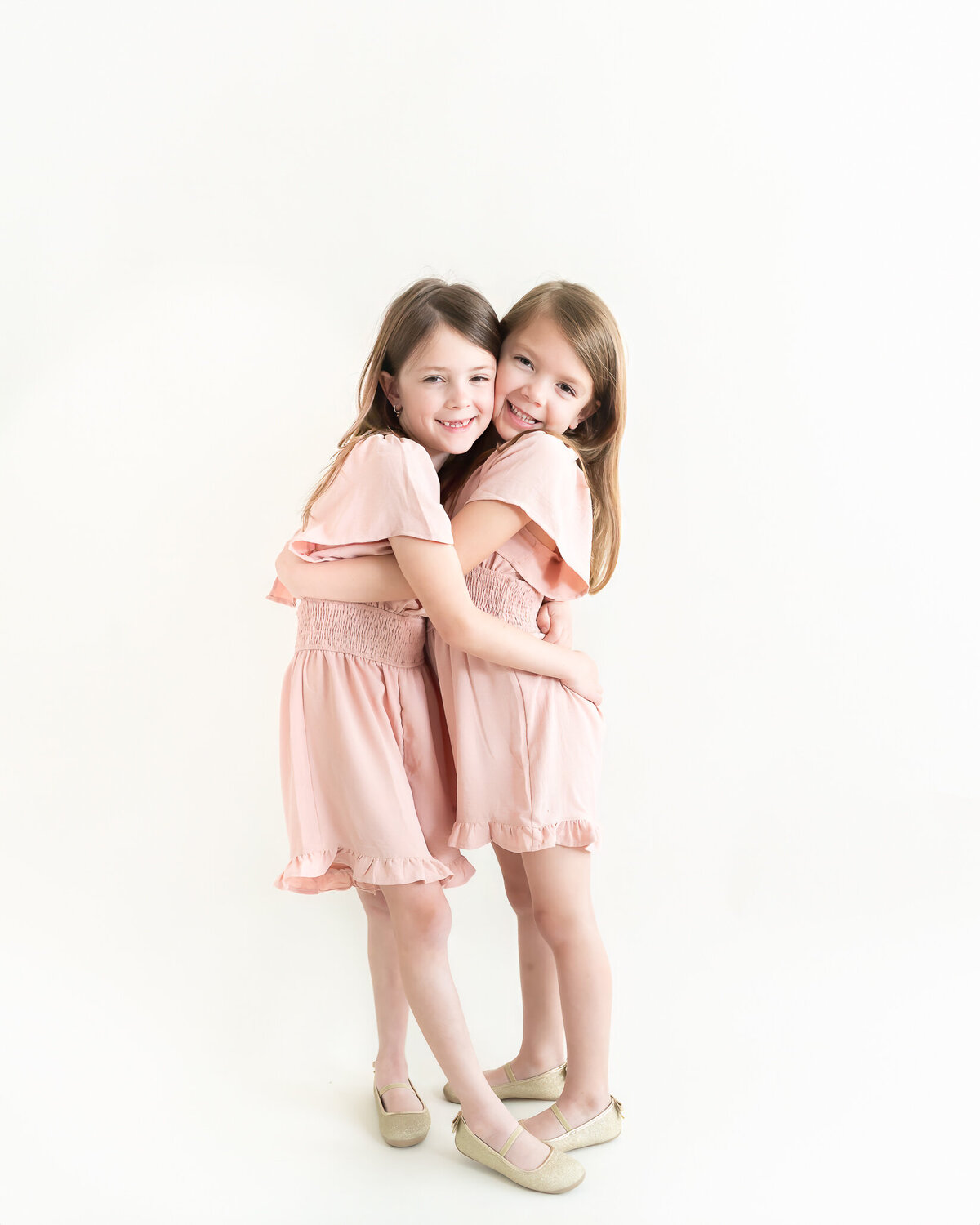studio portrait of little girls in matching pink dresses hugging