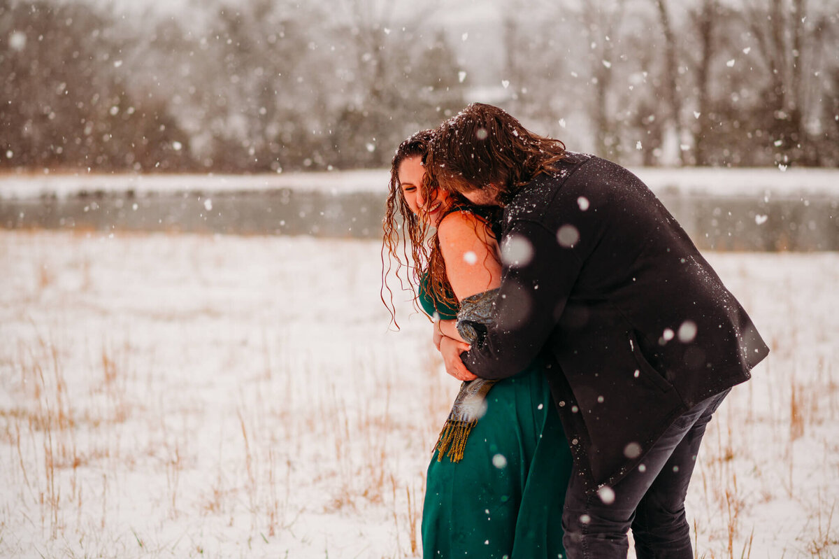 photo of a man hugging a woman in a green dress while it snows
