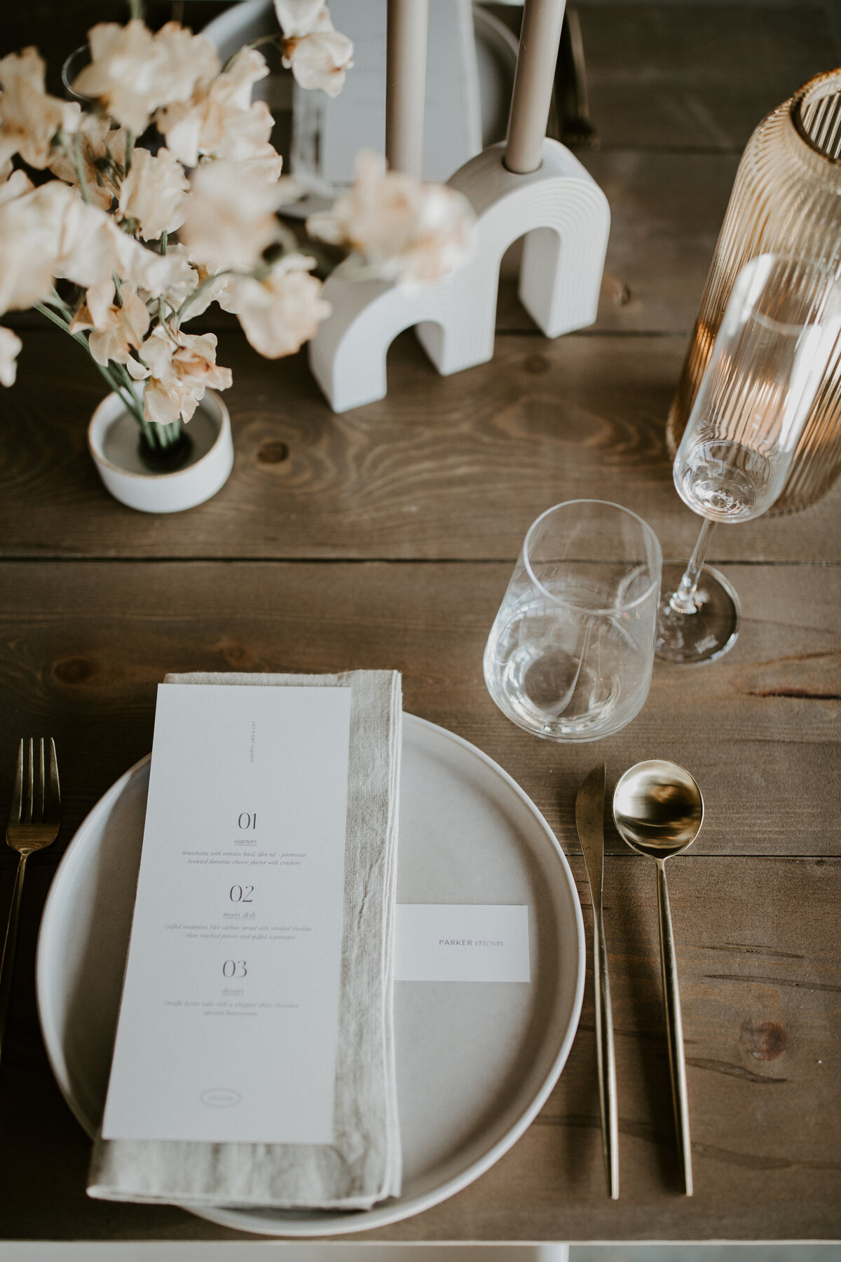 White dinner menu with black font atop a white linen napkin and white plate set on a wooden table.