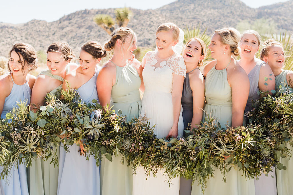 Bride surrounded by her bridal party laughing and holding succulent bouquets in the desert on her wedding day