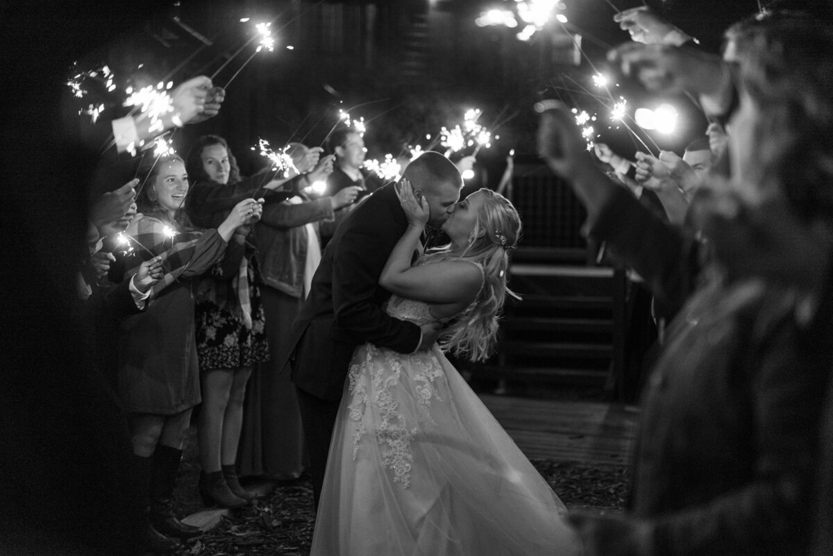 Bride and groom embrace for final kiss underneath sparkler exit at their wedding