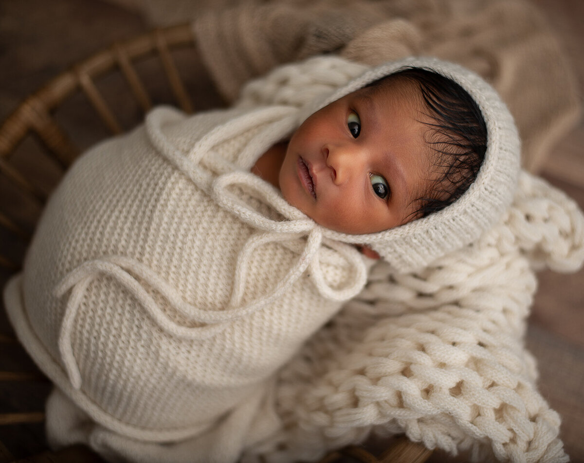 newborn photo of baby looking at camera and wrapped in white in bowl