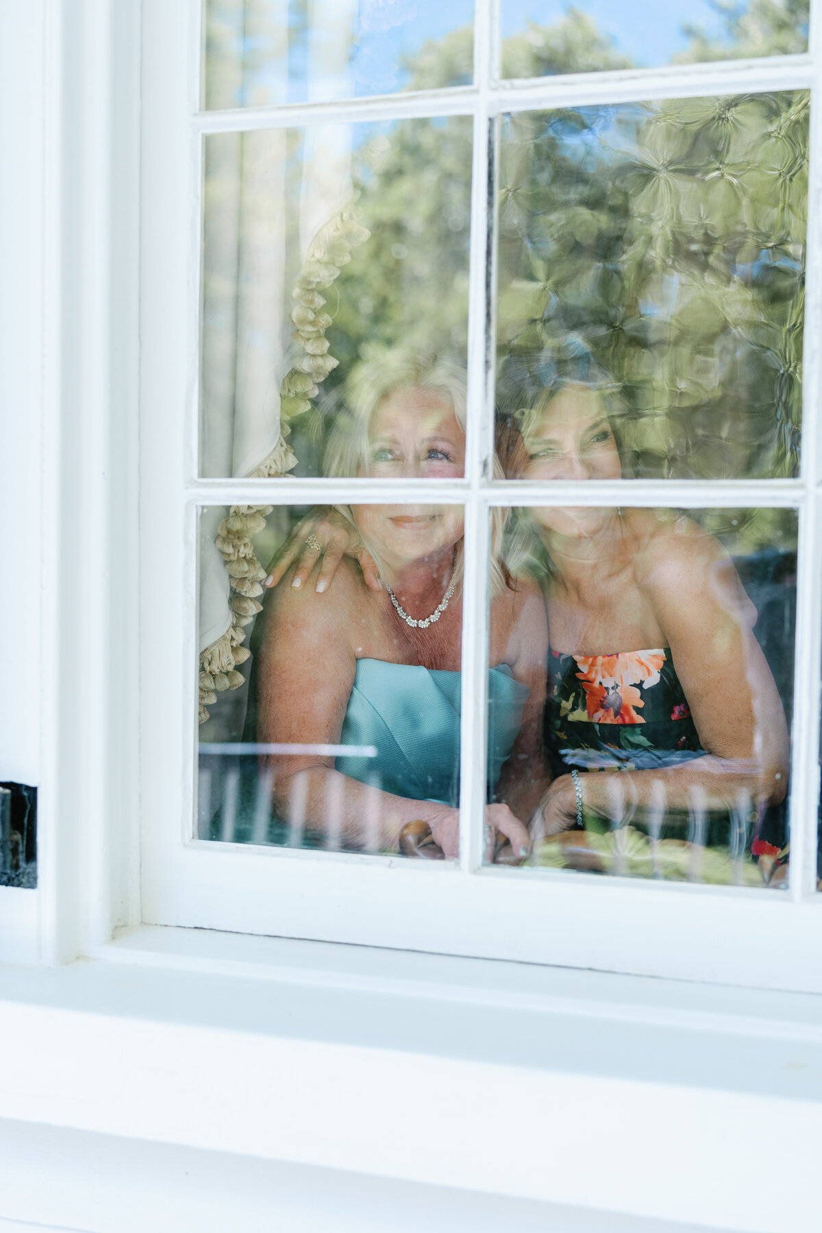 Mothers of the bride and groom watch first look through a window