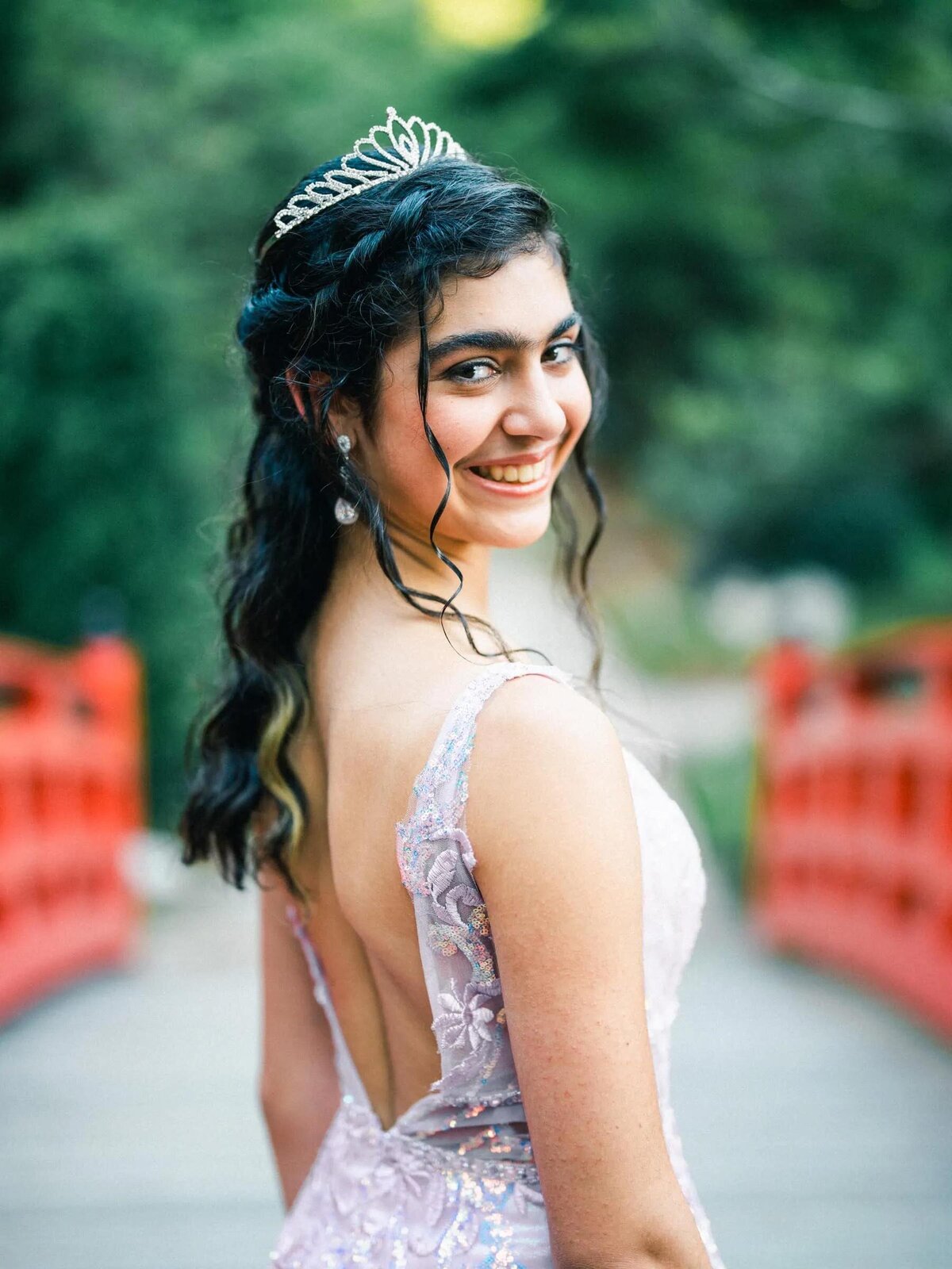 A teenager in a dress and tiara looking over her shoulder.